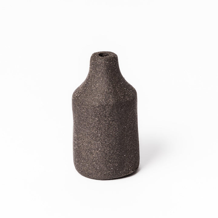 Minimalist dark ceramic bud vase with a cylindrical silhouette and matte finish, perfect for showcasing single stems or dried botanicals.