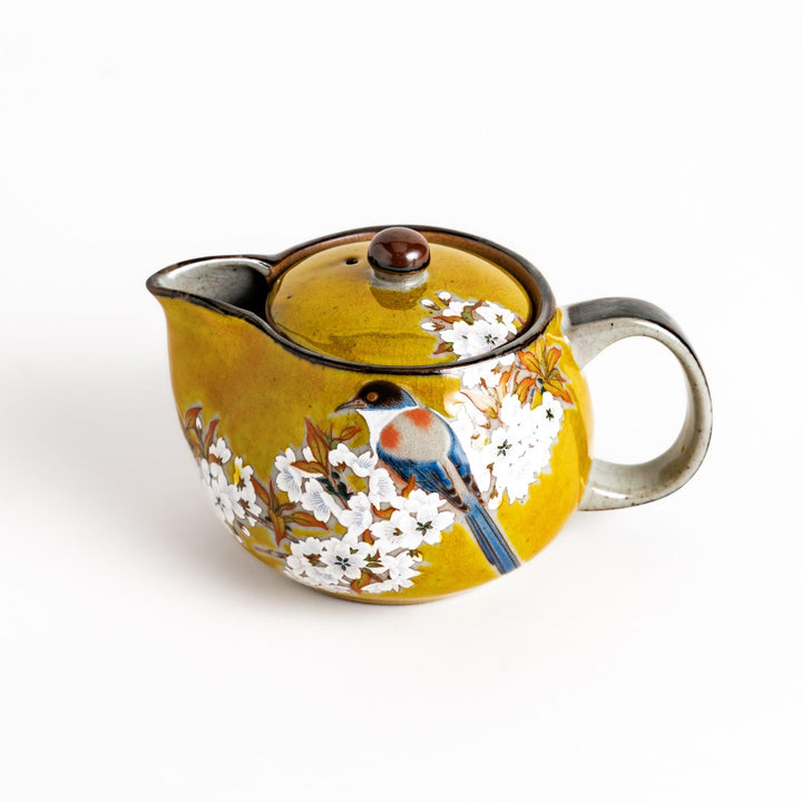 Yellow ceramic teapot with a beautiful bird and flower design, featuring a smooth sheen and secure lid, perfect for serving tea.