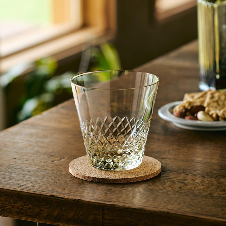 Empty Japanese whiskey glass with a faceted diamond pattern, placed on a cork coaster on a wooden table.