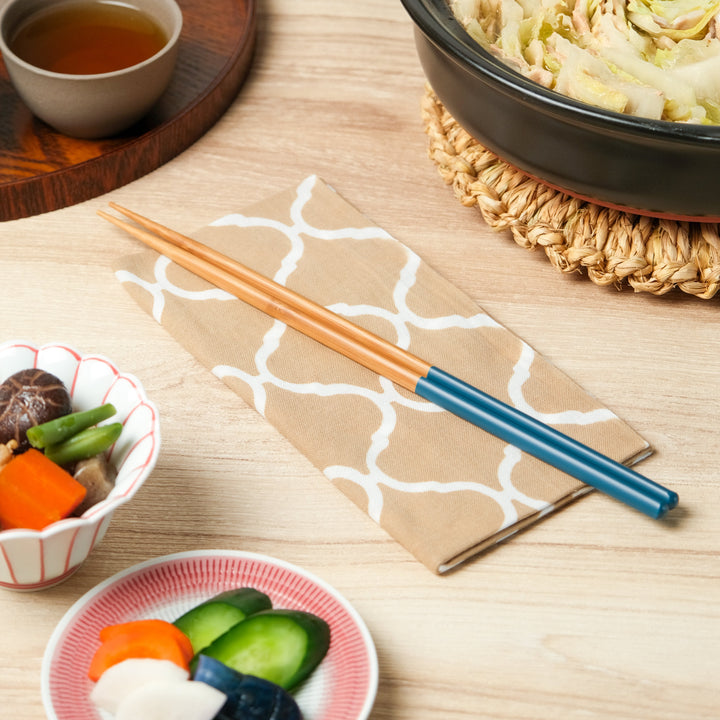 Teal and natural wood Japanese Cooking Chopsticks placed on a patterned beige cloth napkin, arranged beside pickles, simmered vegetables, and a hot pot for a traditional meal.