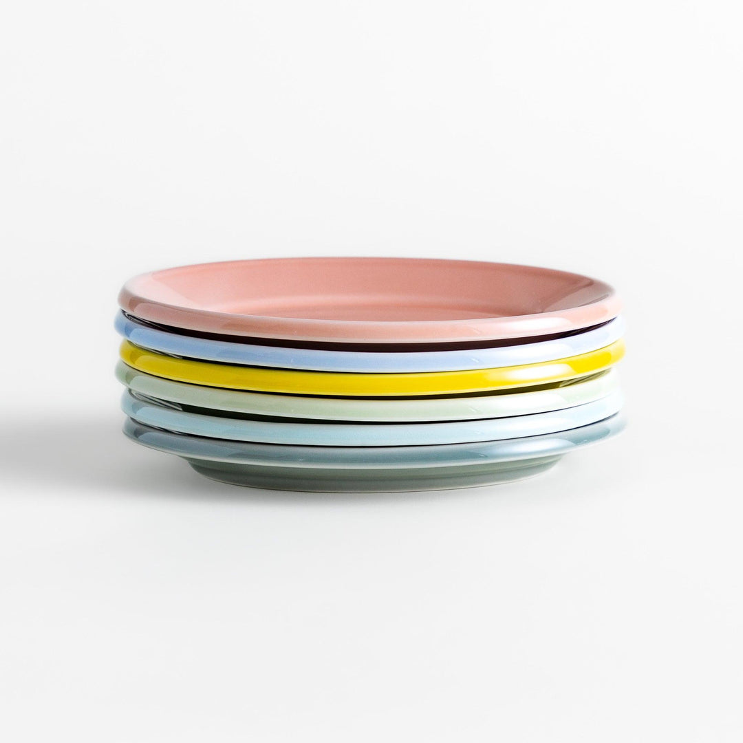 A stack of six pastel-colored oval dessert plates in pink, blue, yellow, green, white, and gray, each with a smooth, glossy finish, perfect for adding a soft, serene touch to your table setting.