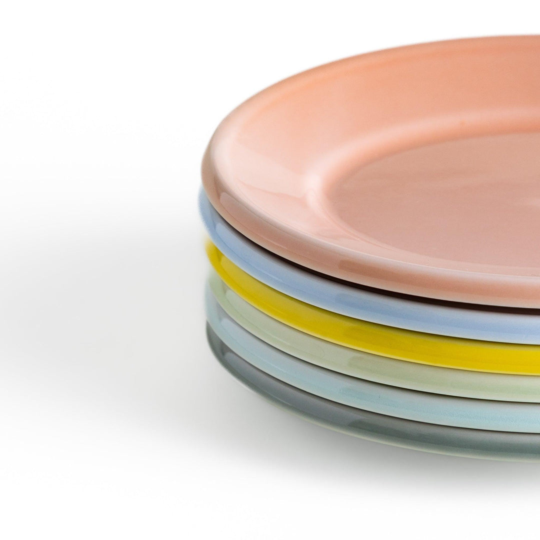 A stack of six pastel-colored oval dessert plates in pink, blue, yellow, green, white, and gray, each with a smooth, glossy finish, perfect for adding a soft, serene touch to your table setting.