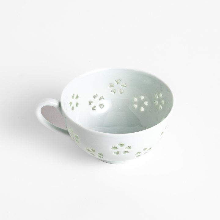 Delicate teacup and saucer set featuring intricate petal-shaped cutouts, allowing light to pass through, creating a soft, elegant design in pale green and white porcelain.