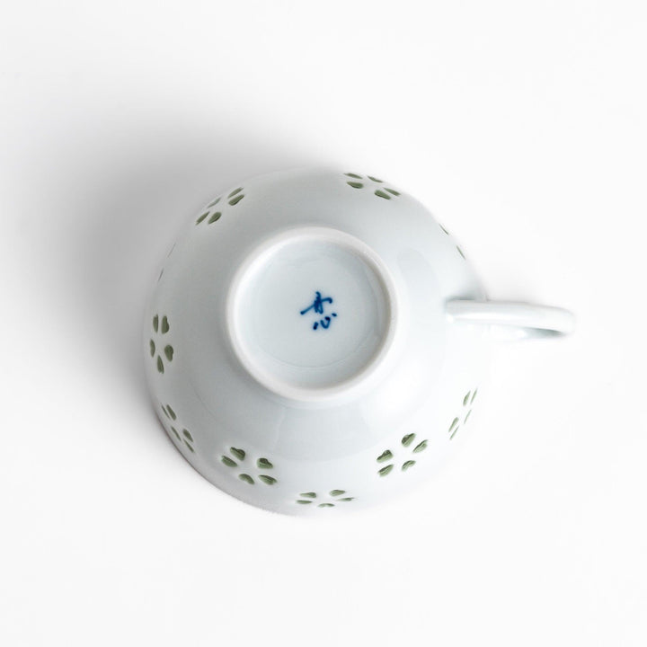 Delicate teacup and saucer set featuring intricate petal-shaped cutouts, allowing light to pass through, creating a soft, elegant design in pale green and white porcelain.
