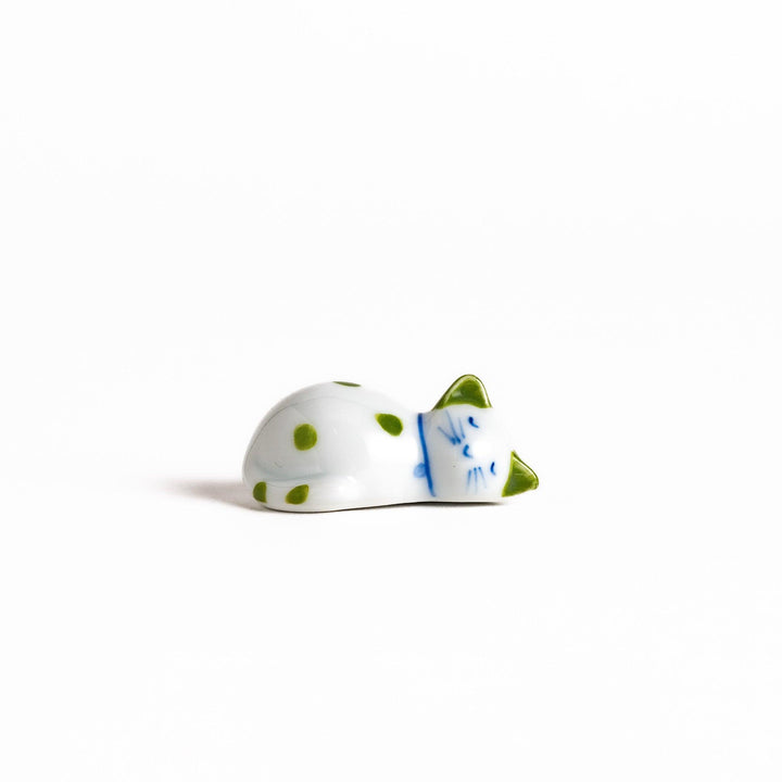 Charming white ceramic chopstick rest shaped like a sleeping cat with green dots, bringing a touch of nature to your table setting.