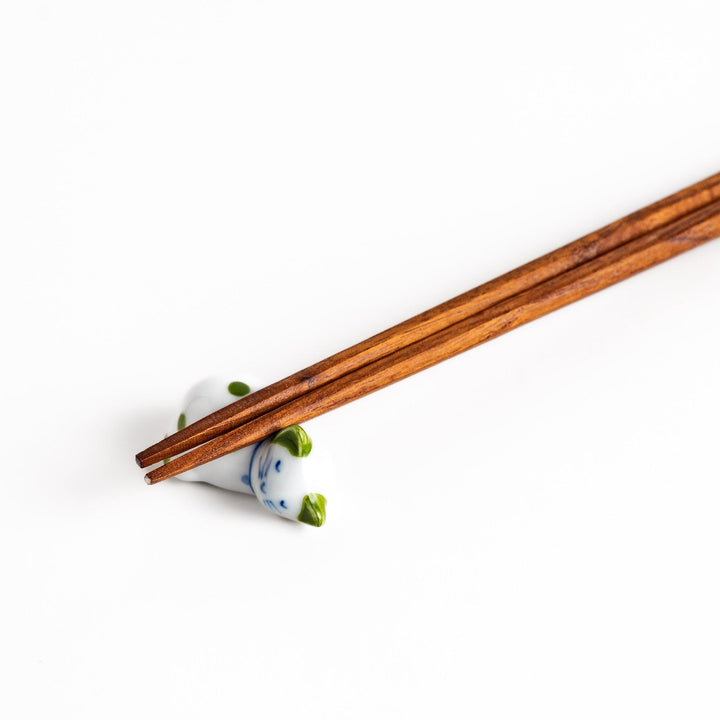 Wooden chopsticks gracefully placed on an adorable white ceramic chopstick rest in the shape of a sleeping cat with green dots.