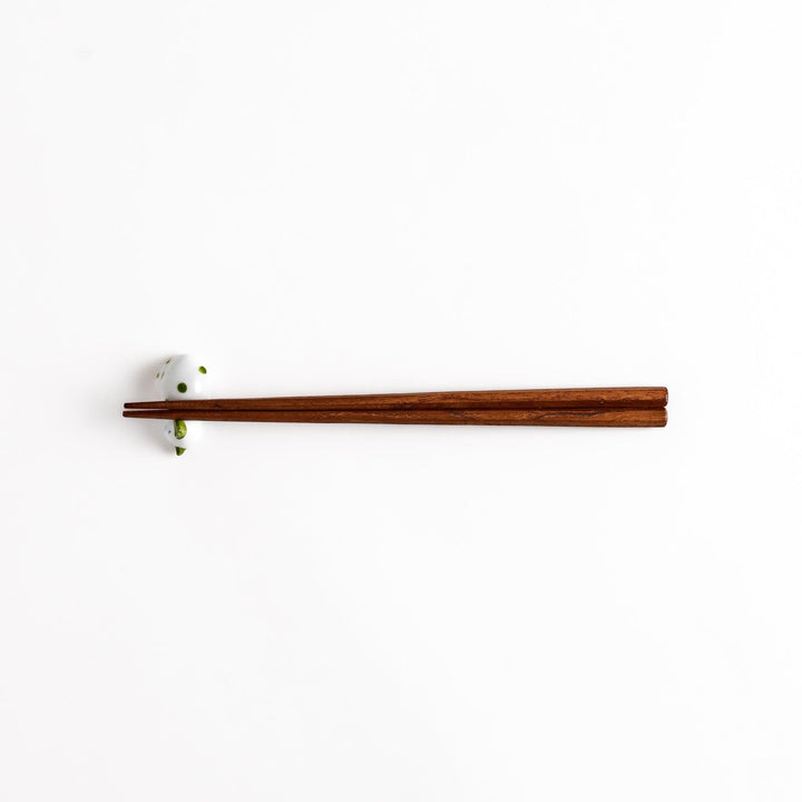 Wooden chopsticks gracefully placed on an adorable white ceramic chopstick rest in the shape of a sleeping cat with green dots.