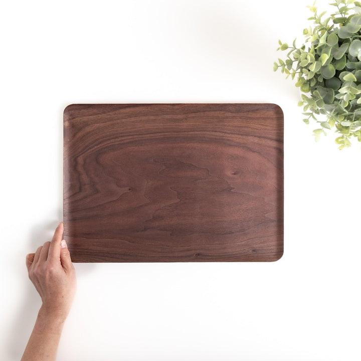 Hand holding a rectangular walnut tray with a rich wood grain, perfect for serving food and drinks or adding a touch of natural elegance to your home decor.