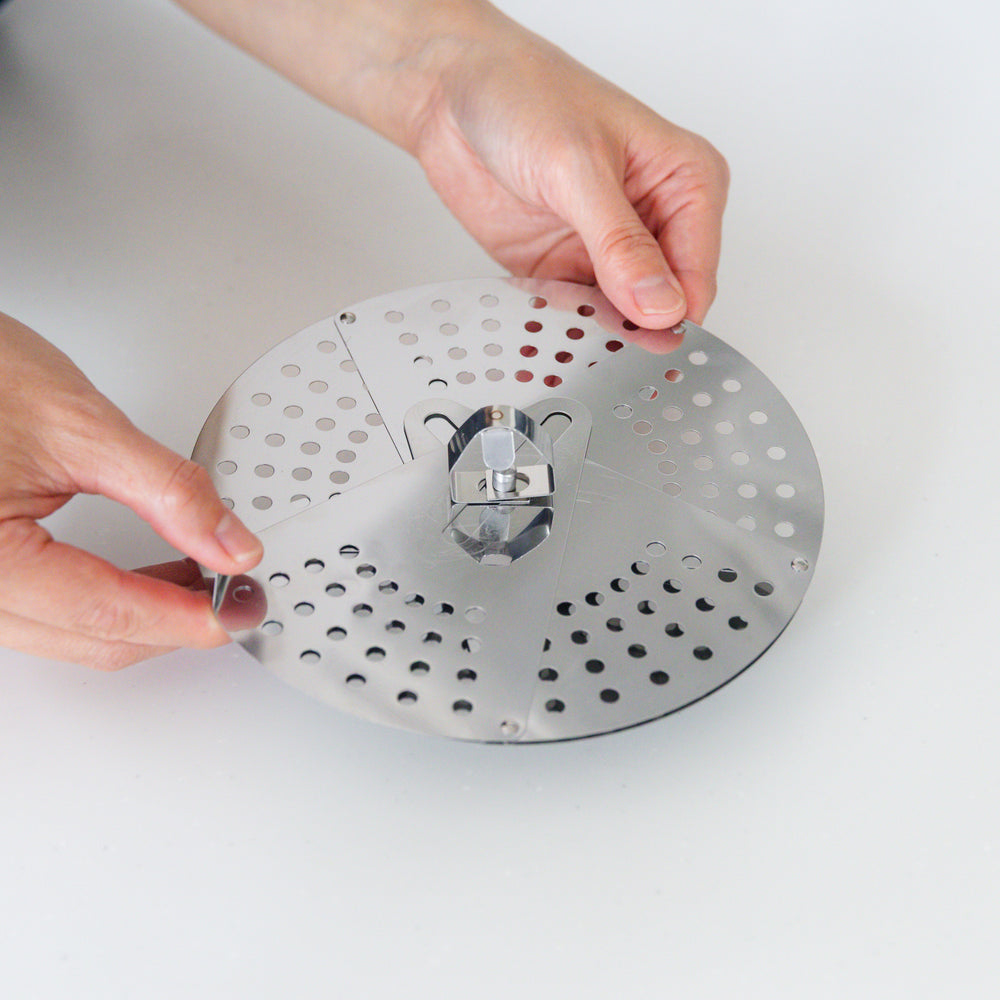 Hand adjusting a stainless steel drop lid with foldable petals, a versatile kitchenware tool for steaming and simmering in various pot sizes.