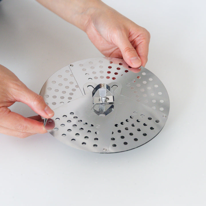 Hand adjusting a stainless steel drop lid with foldable petals, a versatile kitchenware tool for steaming and simmering in various pot sizes.