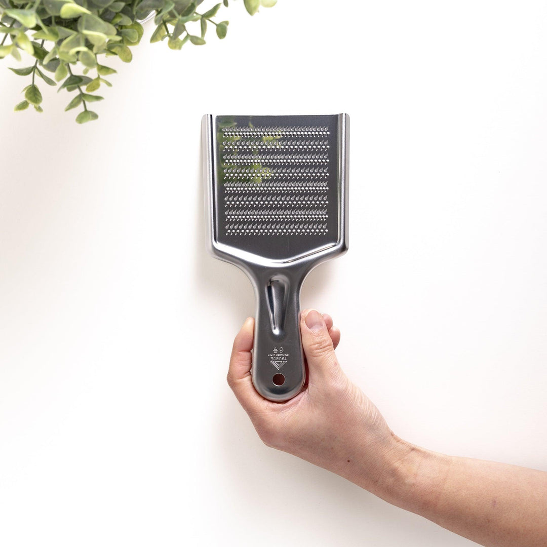 Hand holding a stainless steel grater with sharp blades on both sides, a versatile kitchenware tool for grating various ingredients with different textures.