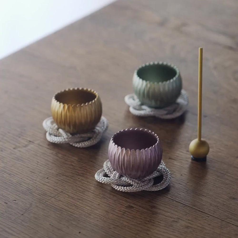Three small brass meditation bowls in gold, green, and purple, played with a stick to create gentle resonant tones.