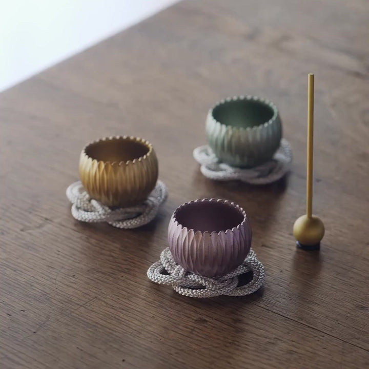 Three small brass meditation bowls in gold, green, and purple, played with a stick to create gentle resonant tones.