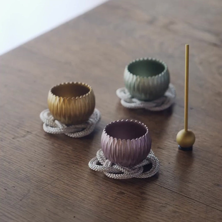 Three small brass meditation bowls in gold, green, and purple, played with a stick to create gentle resonant tones.