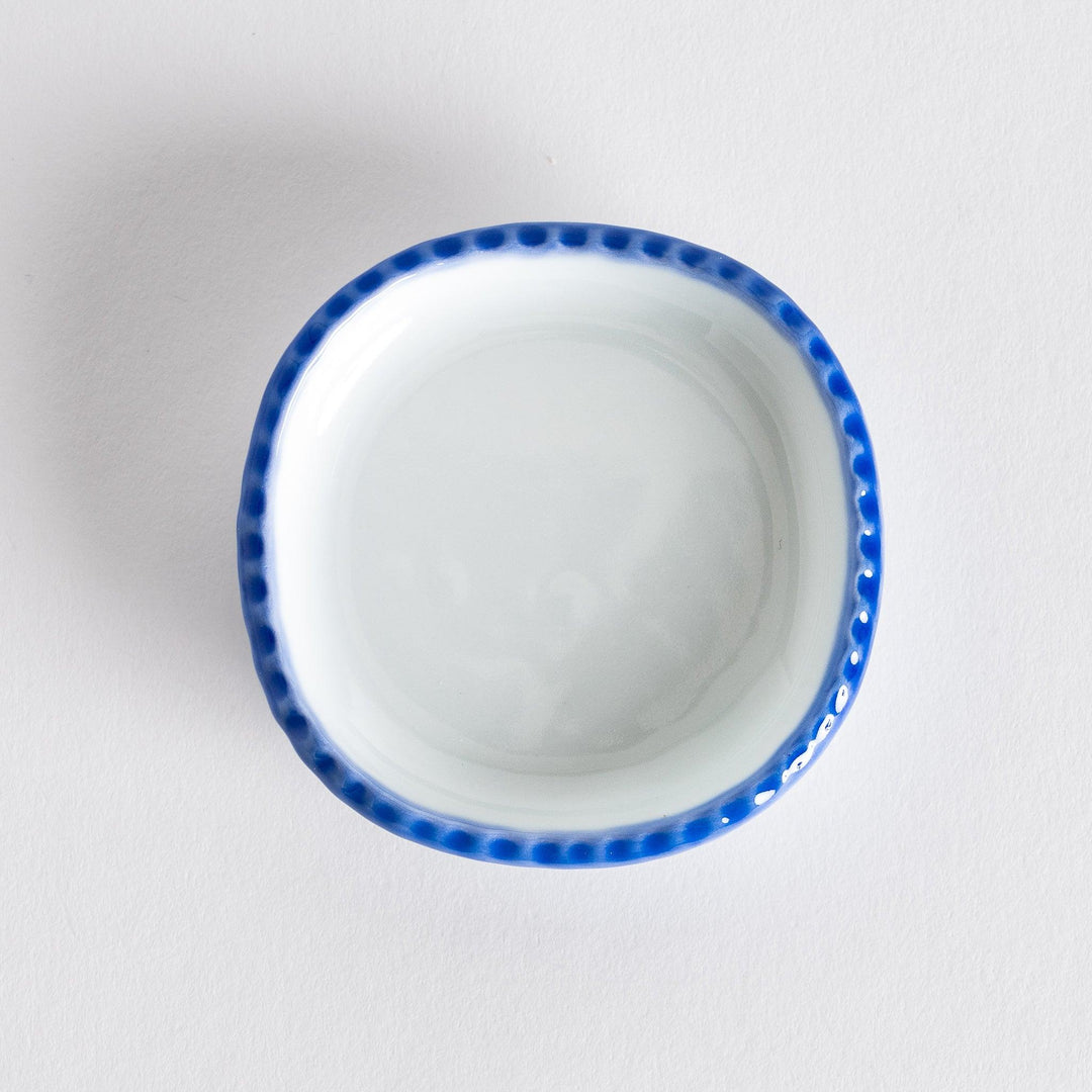 Top view of an oval sauce dish featuring a rustic scalloped edge with blue detailing along the rim.