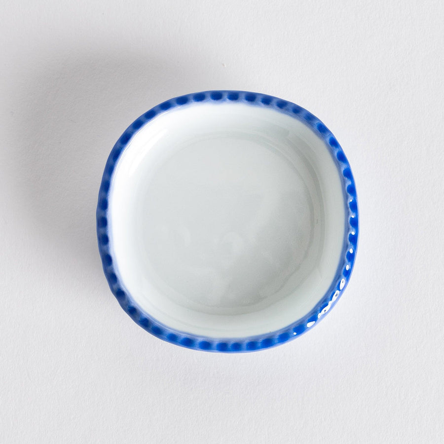 Top view of an oval sauce dish featuring a rustic scalloped edge with blue detailing along the rim.