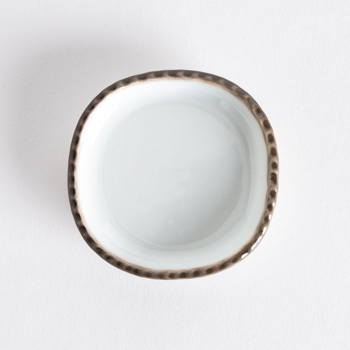 Top view of a small oval sauce dish featuring a scalloped edge and a brown dotted rim.