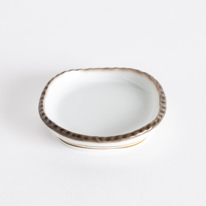Side view of a small oval sauce dish with a brown dotted rim and smooth interior.