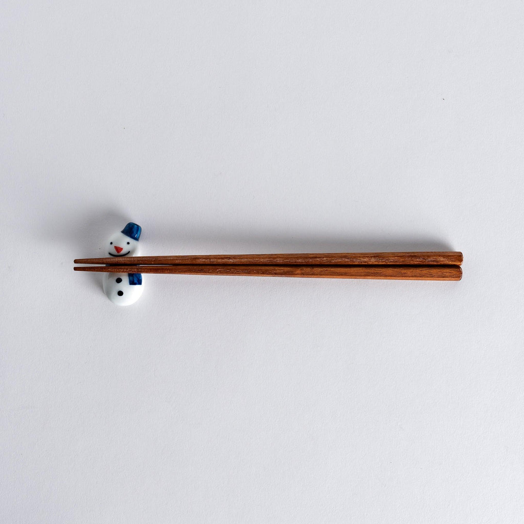 Full view of snowman chopstick rest with chopsticks resting on it, showcasing the playful snowman design with a blue hat and scarf.