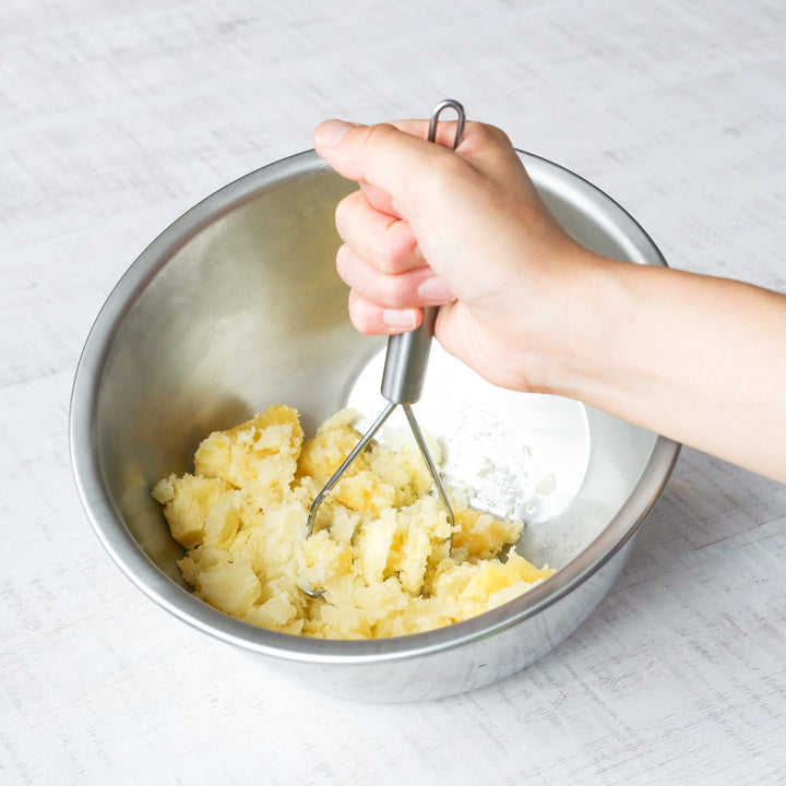 Mashing cooked potatoes in a stainless steel mixing bowl, great for preparing creamy mashed potatoes or potato salad.