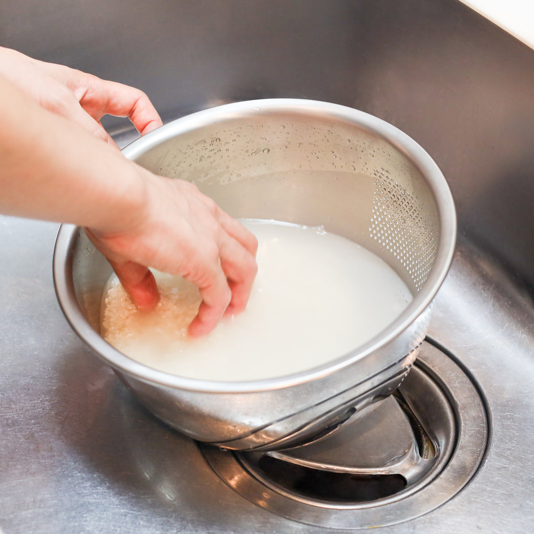 Rinsing Japanese rice in a stainless steel colander set over a bowl, perfect for efficient prep before cooking fluffy rice dishes.