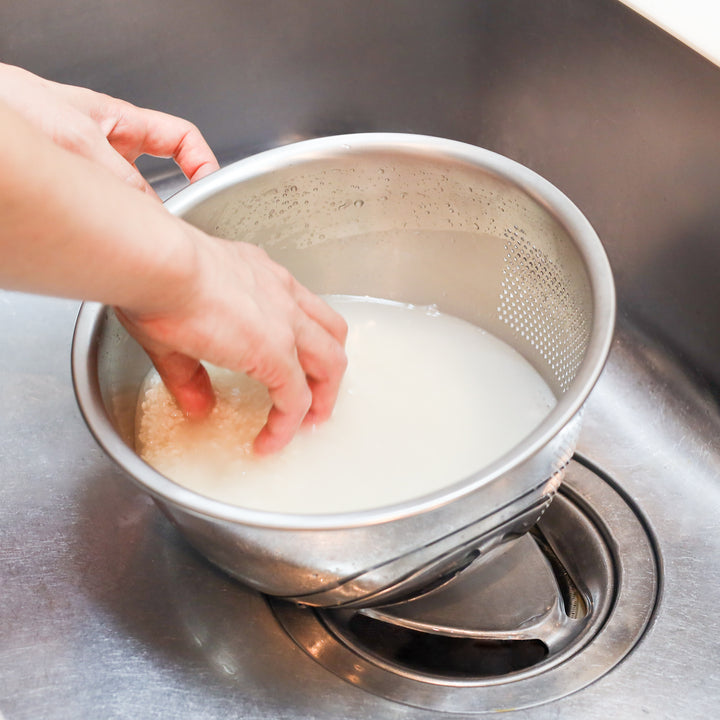 Rinsing Japanese rice in a stainless steel colander set over a bowl, perfect for efficient prep before cooking fluffy rice dishes.
