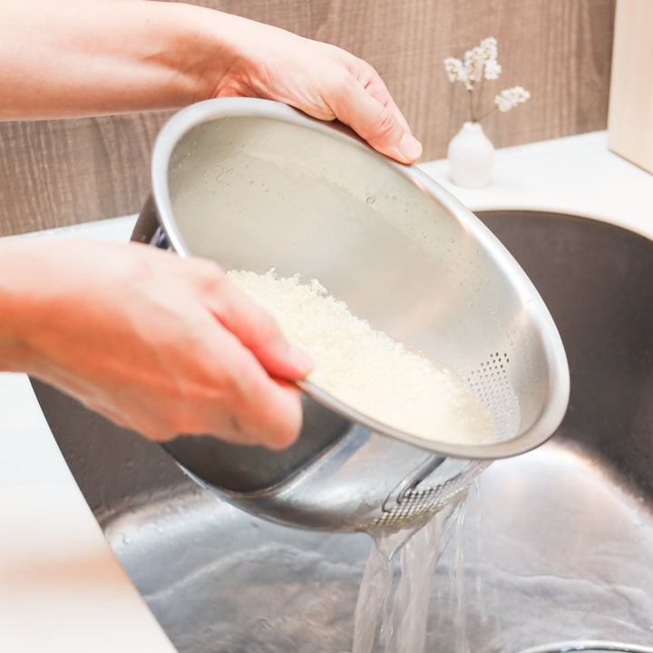 Draining rinsed Japanese rice using a stainless steel colander, ideal for reducing excess water before cooking.
