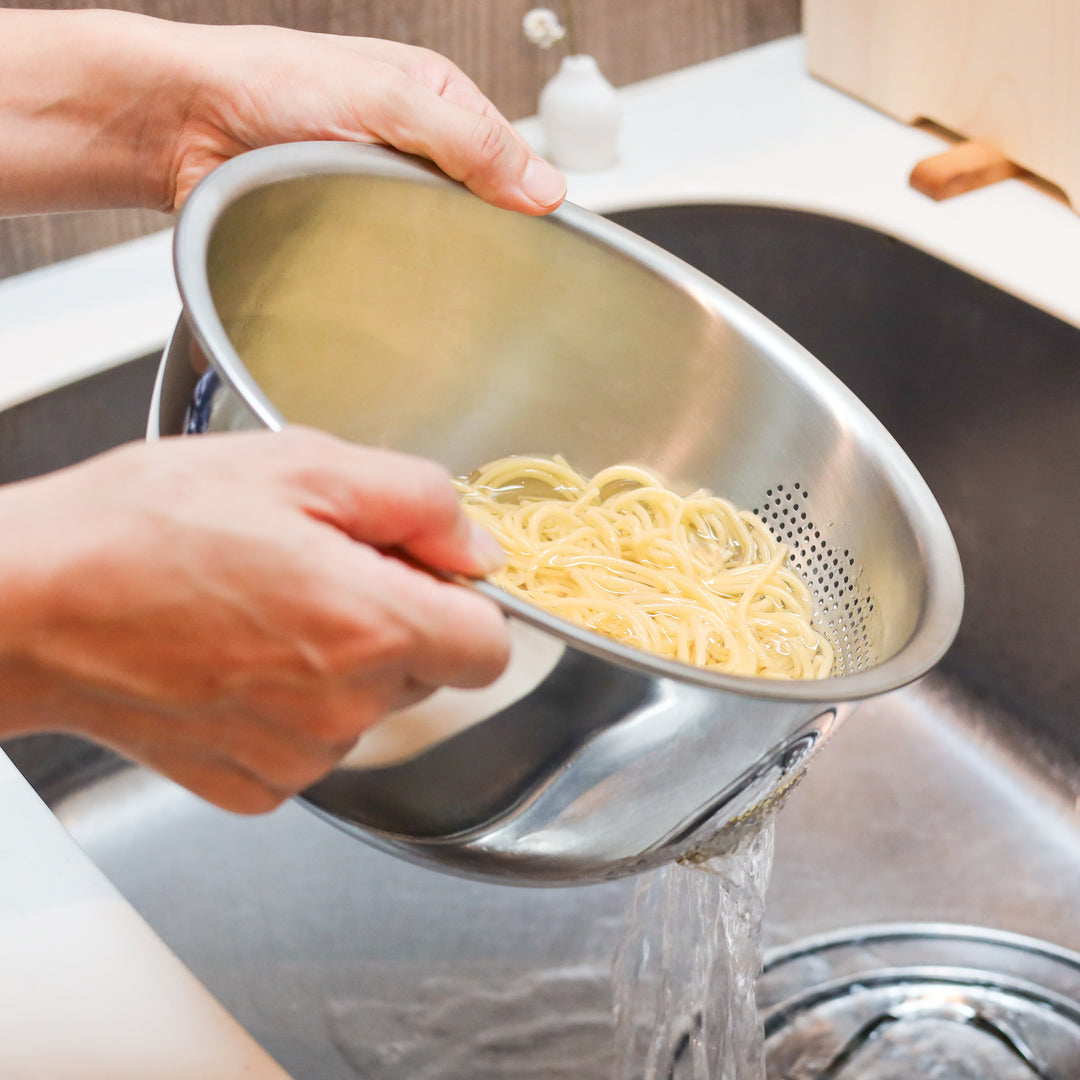 Draining cooked spaghetti with a stainless steel colander bowl in the sink, showing a clean and efficient way to strain pasta.
