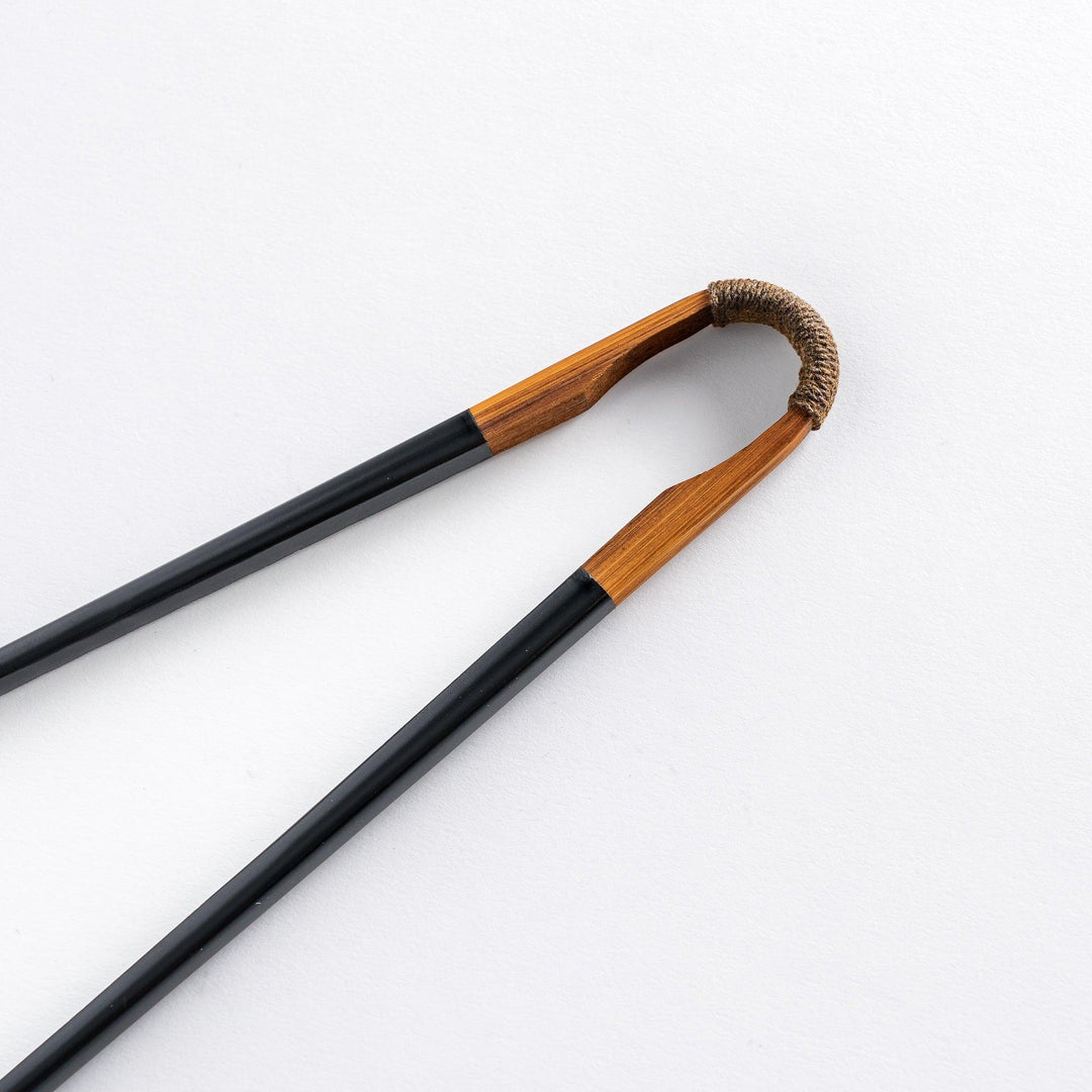 Close-up of the curved tip of a black lacquered chopstick, with the wooden handle and twine detail.