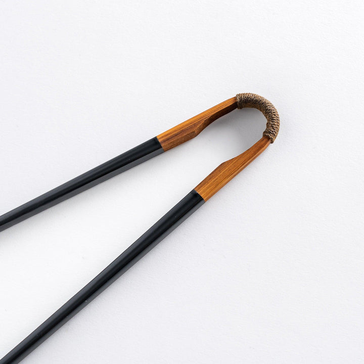 Close-up of the curved tip of a black lacquered chopstick, with the wooden handle and twine detail.