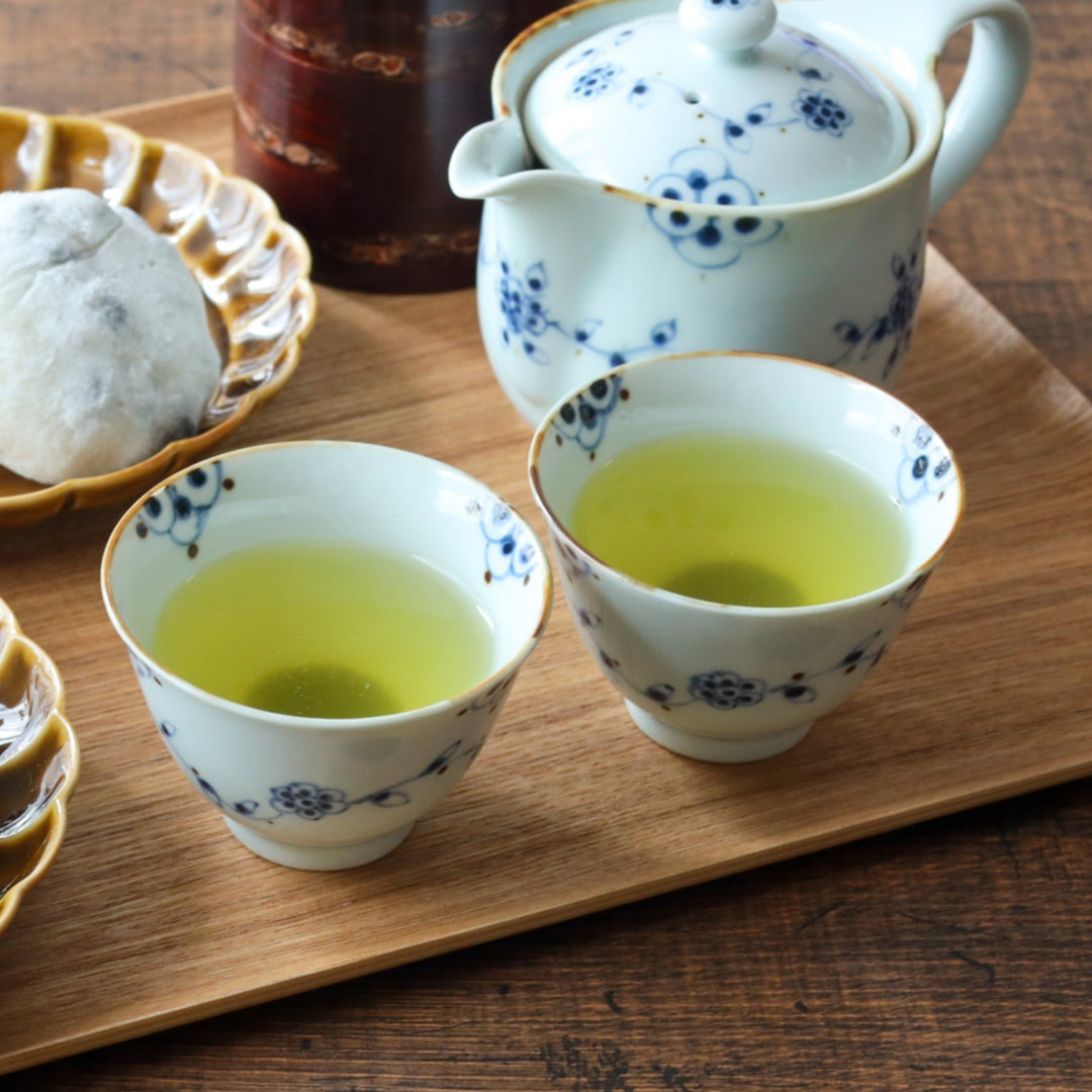 White porcelain teacup with blue floral vine patterns and gold-rim accents, paired with green tea for a serene, traditional setting.