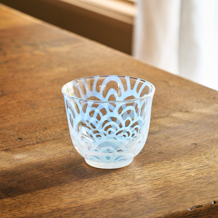 A vintage-style glass tea cup featuring a light blue art deco pattern, set on a wooden table in natural light.