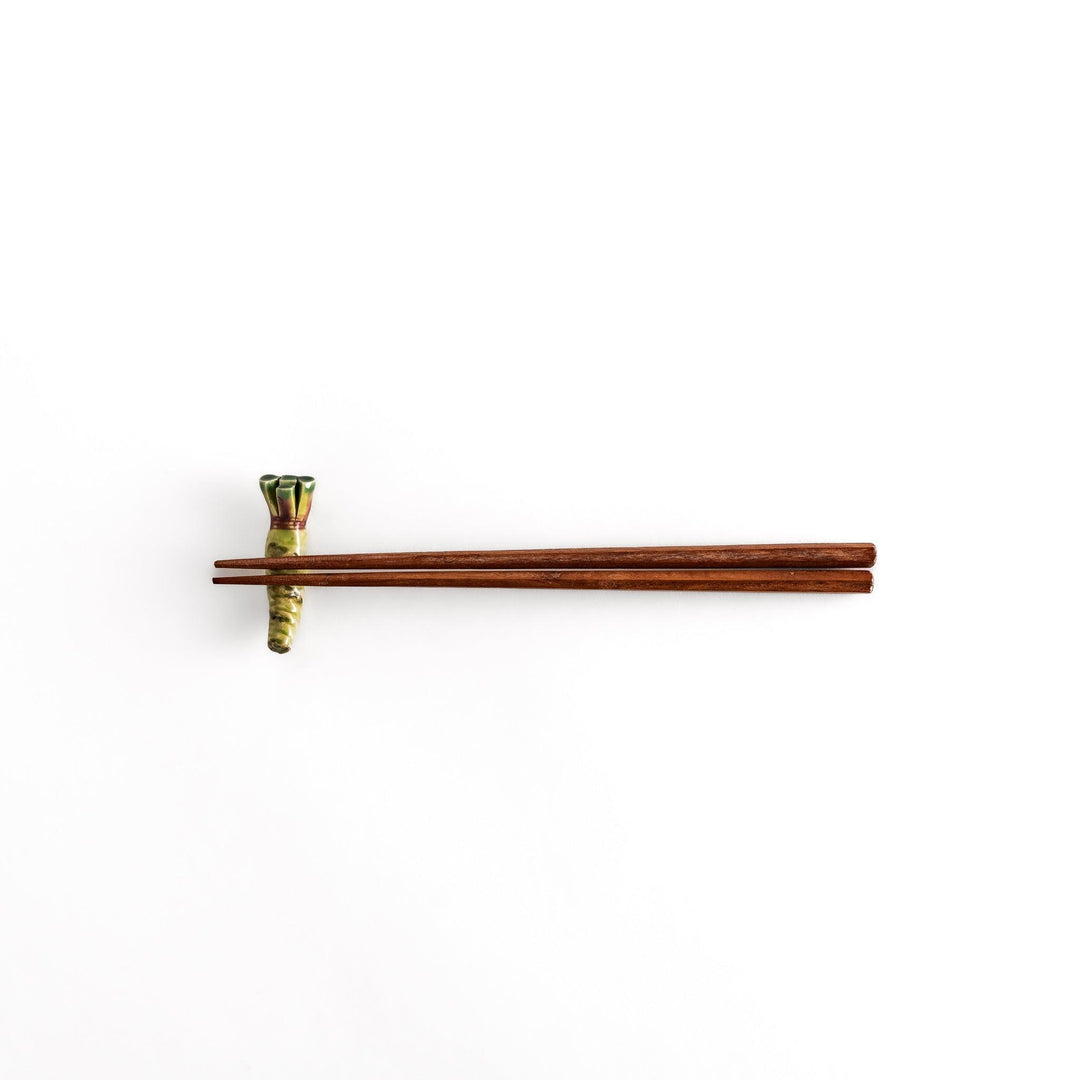 Wooden chopsticks delicately balanced on the ceramic wasabi chopstick rest, highlighting its realistic design and functional elegance.