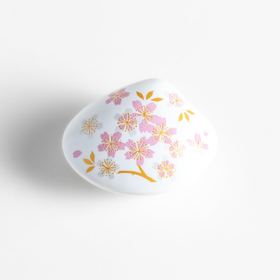 White ceramic incense holder shaped like a seashell, adorned with delicate pink and gold cherry blossoms, featuring a sakura-shaped holder for a refined touch.