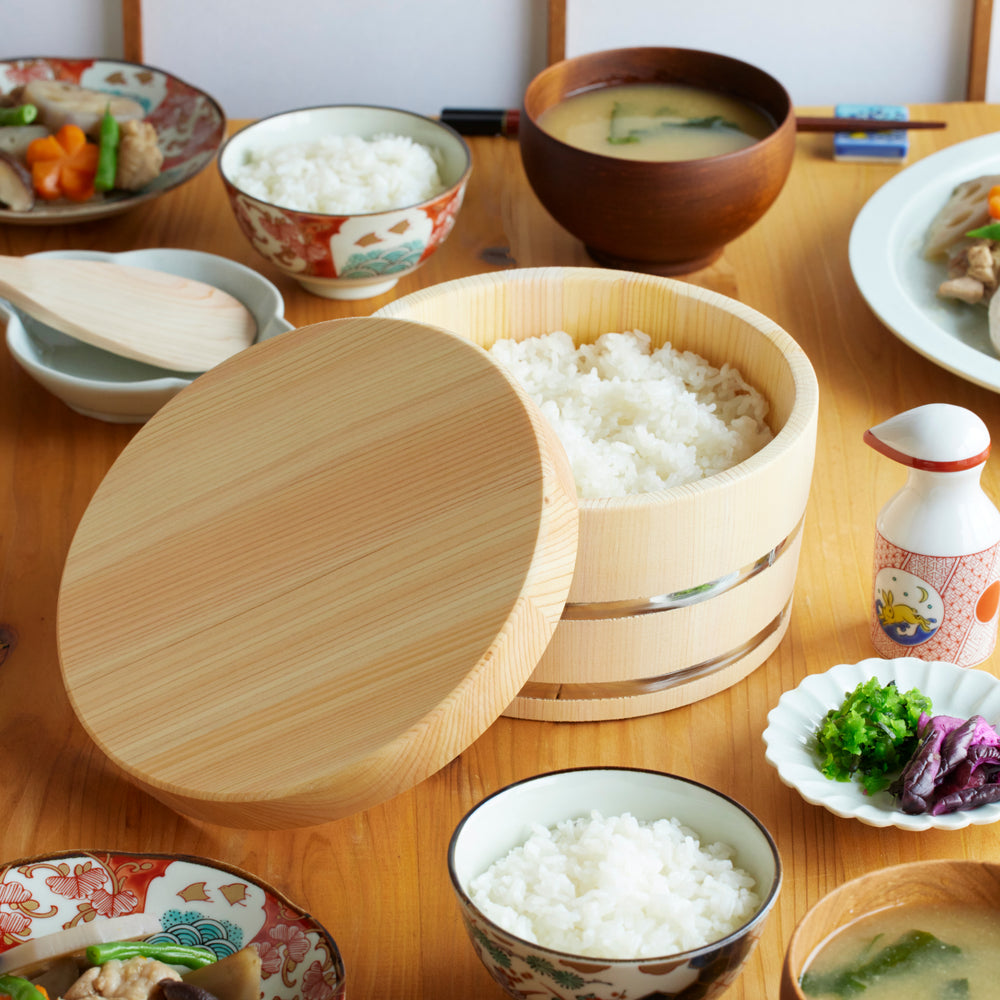 Wooden ohitsu rice storage bowl filled with freshly cooked rice, placed on a Japanese dining table with miso soup and side dishes.